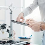 Mechanical engineers in the laboratory using a 3D printer for testing and prototyping, the are checking a list on a clipboard