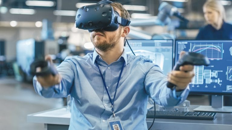 Portrait Shot of the Industrial Engineer Wearing Virtual Reality Headset and Using Controllers, ready to Work. In the Background Manufacturing Plant and Monitors.